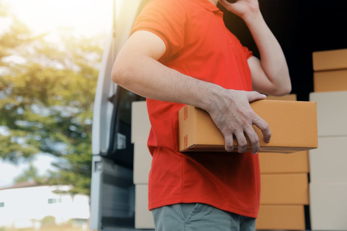 Courier handing boxes to a customer at their front door while wearing a protective face mask
