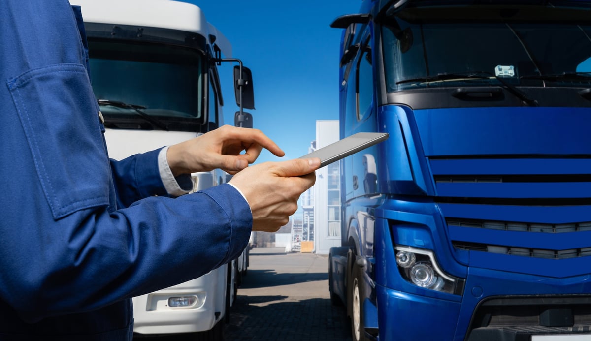 Fleet manager reviewing routes on a tablet in front of a line of delivery trucks