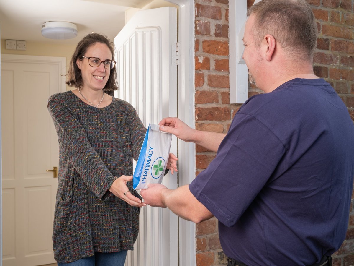 Courier handing a pharmacy prescription package to a patient at the doorway of a home
